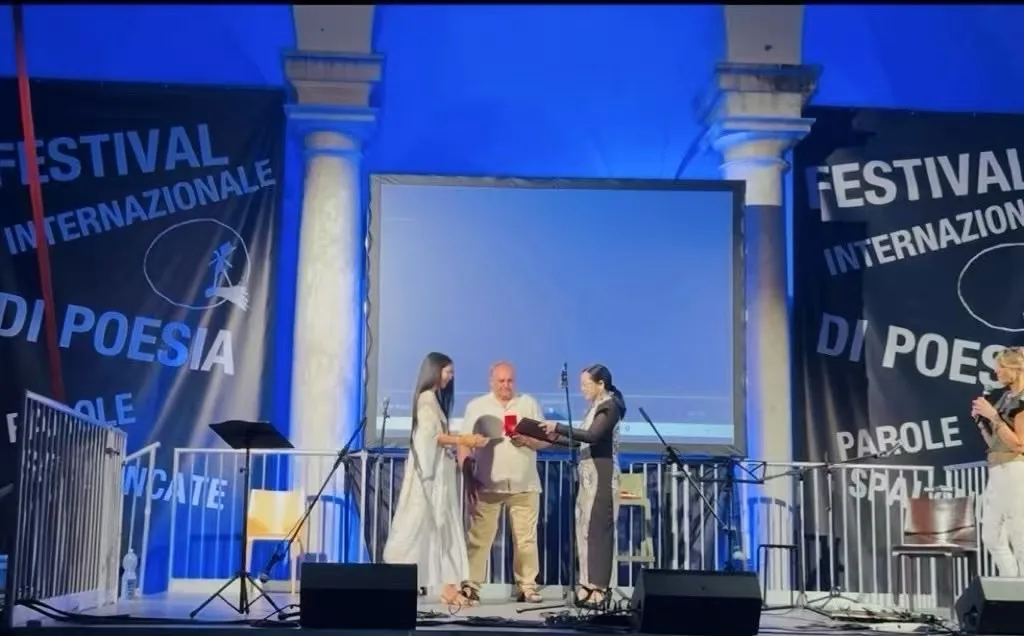 Sula on stage at the Genoa Poetry Festival alongside fellow poets and the festival director